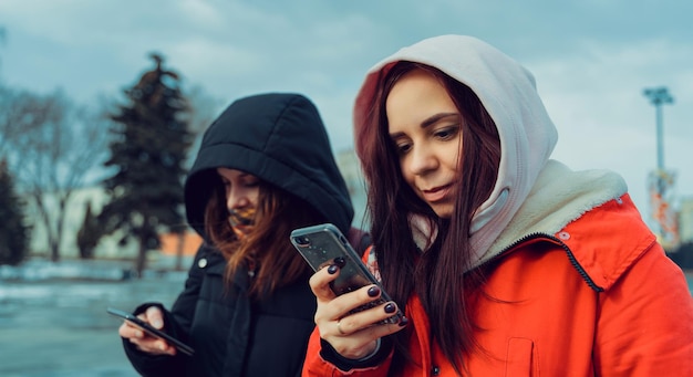 Close-up de mulheres jovens navegando em smartphone no parque da cidade Mulheres bonitas em capuzes usando telefone celular