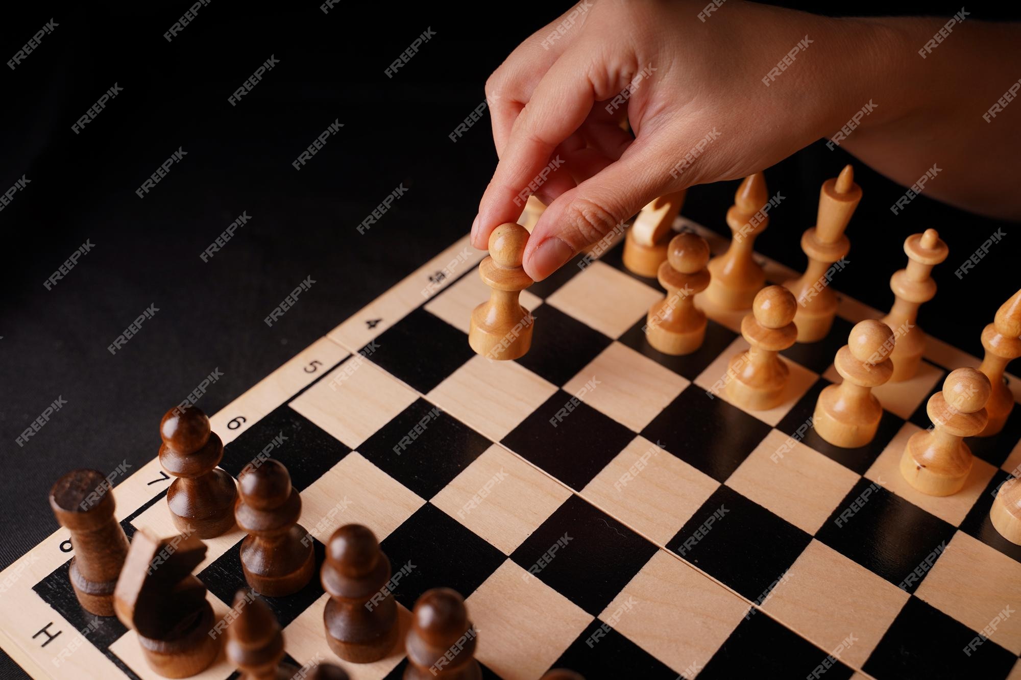 Close-up de peças de xadrez de madeira brancas e pretas a bordo a mão da  mulher faz o primeiro movimento do peão branco no tabuleiro de xadrez  conceito de jogo lógico e