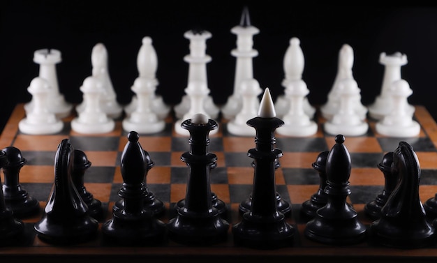 Foto close-up de peças de xadrez pretas opostas às brancas ao longo do tabuleiro em fundo preto isolado