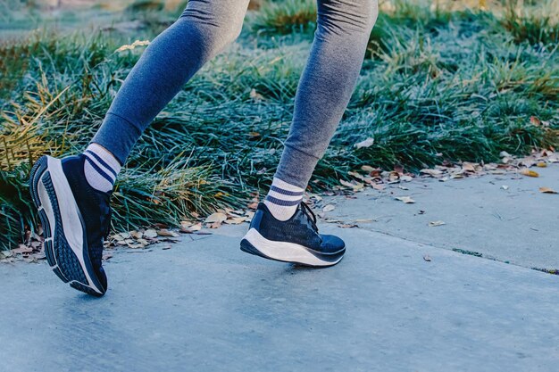 Close-up de pés masculinos em sapatos de treino indo correr na rua com folhas amarelas no chão