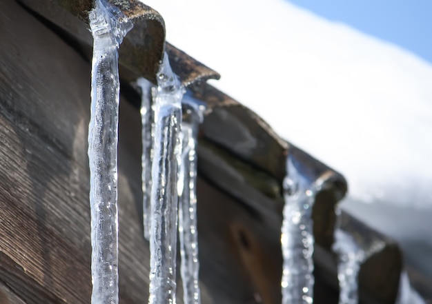 Close-up de pingentes de gelo transparentes brilhantes pendurados em um telhado.