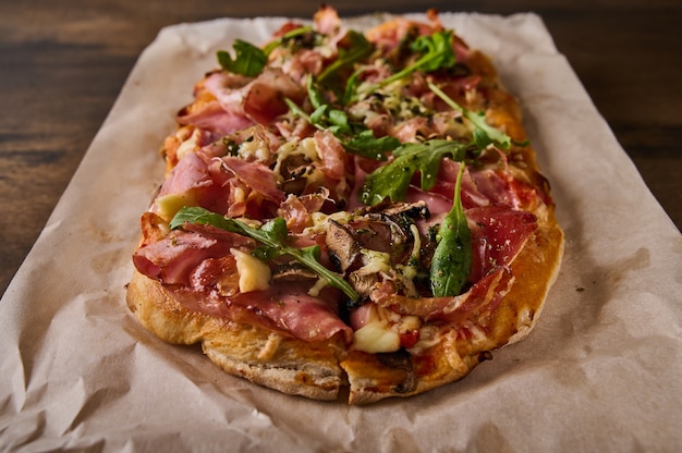 Close up de pizza romana retangular com presunto, tomate, mussarela, cogumelos e rúcula