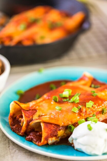 Close up de prato de jantar com enchiladas de frango guarnecido com cebolinha e creme de leite.