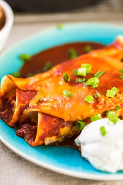 Close up de prato de jantar com enchiladas de frango guarnecido com cebolinha e creme de leite.