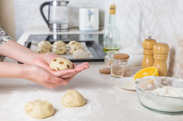 Close-up de preparar e formar bolos de Páscoa Cruz com passas de massa. Mãos femininas, amassar massa na cozinha minimalista moderna.