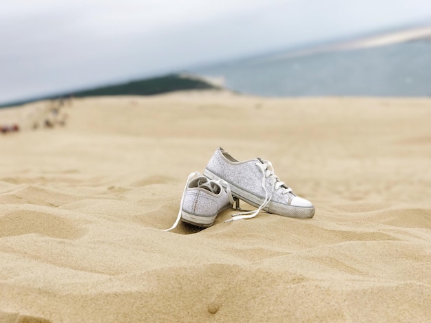 Close-up de sapatos na areia na praia contra o céu