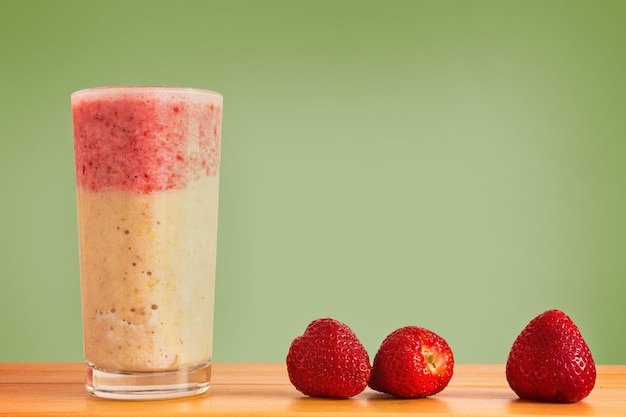 Foto close-up de smoothie de morango e banana em mesa de madeira contra fundo verde