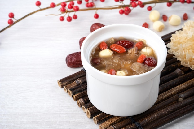 Close-up de sopa tradicional chinesa de fungos brancos e doces com sementes de lótus, tâmaras vermelhas, jujube e goji berry em fundo branco