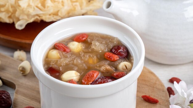 Close-up de sopa tradicional chinesa de fungos brancos e doces com sementes de lótus, tâmaras vermelhas, jujube e goji berry em fundo branco