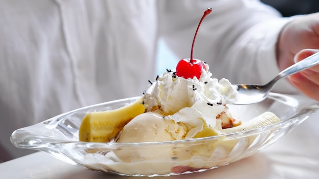 Foto close-up de sorvete com chantilly, banana e cereja.