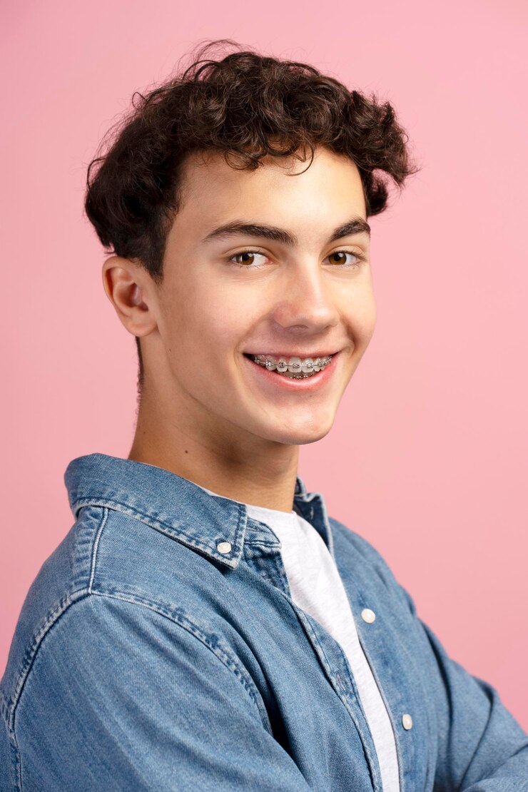 Foto close-up de um adolescente feliz e atraente com aparelhos ortopédicos vestindo roupas casuais em fundo rosa