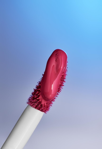 close-up de um aplicador de brilho labial contra um fundo azul de gradiente fresco