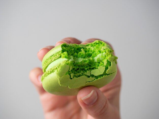 Close-up de um biscoito de macaroon verde mordiscado na mão em um fundo branco