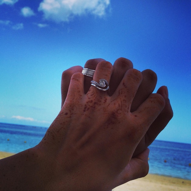 Foto close-up de um casal com anéis de mãos dadas na praia contra o céu