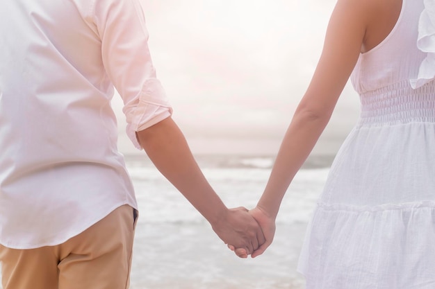 Close-up de um casal de vestido branco de mãos dadas na praia