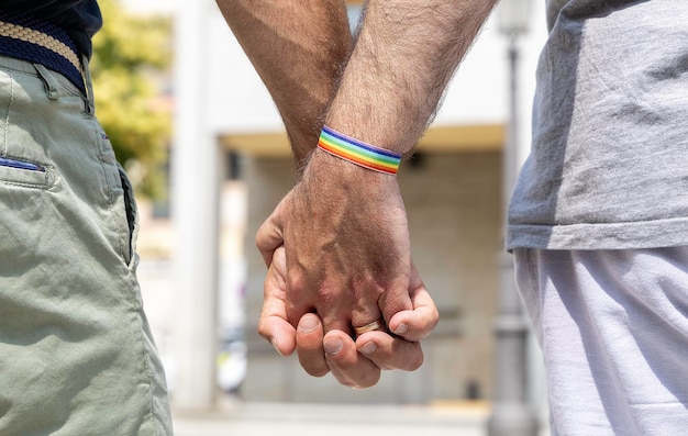 Foto close-up de um casal gay masculino de mãos dadas com uma pulseira de arco-íris em um pulso conceito de orgulho gay