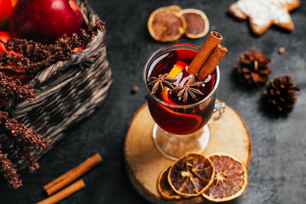 Foto close-up de um copo com vinho quente canela e cardamomo em um fundo preto com ingredientes para a bebida