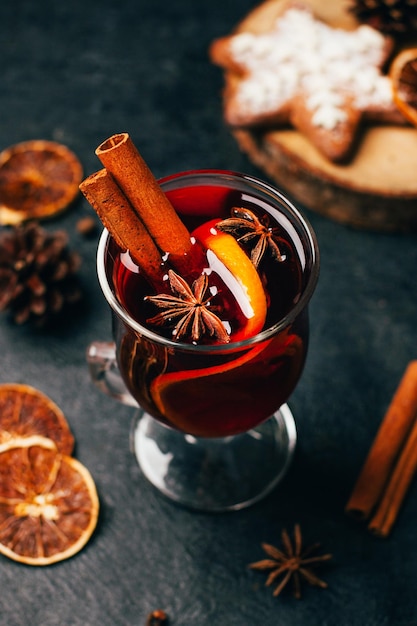 Foto close-up de um copo com vinho quente canela e cardamomo em um fundo preto com ingredientes para a bebida