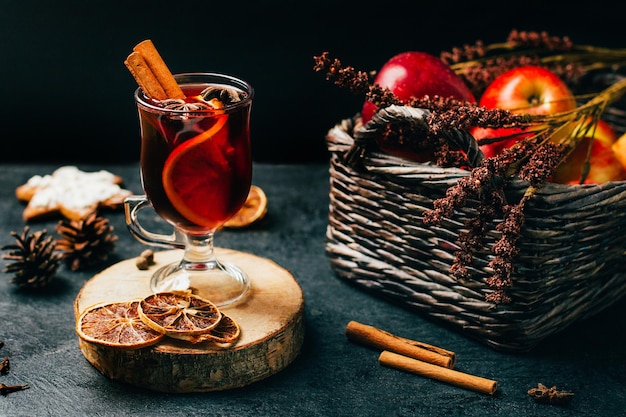 Foto close-up de um copo com vinho quente canela e cardamomo em um fundo preto com ingredientes para a bebida