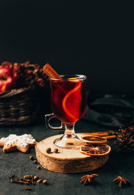 Foto close-up de um copo com vinho quente canela e cardamomo em um fundo preto com ingredientes para a bebida