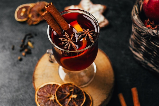 Foto close-up de um copo com vinho quente canela e cardamomo em um fundo preto com ingredientes para a bebida