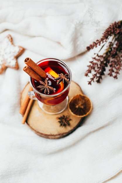 Close-up de um copo de vinho quente com varas de canela e cardamomo em um fundo branco