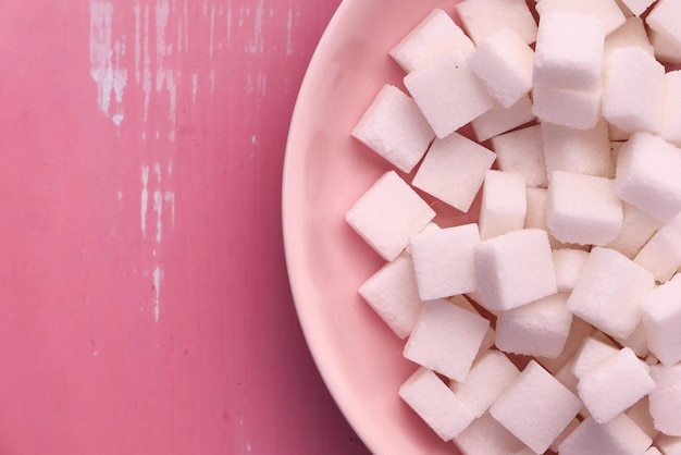 Foto close-up de um cubo de açúcar em um prato em fundo rosa