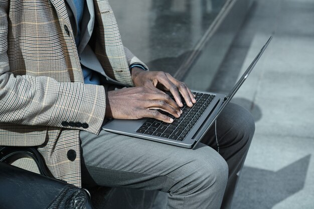 Close-up de um empresário africano trabalhando em um laptop on-line ao ar livre