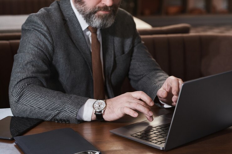 Close-up de um empresário barbudo maduro digitando no laptop e trabalhando on-line enquanto está sentado à mesa no café