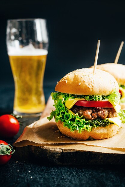 Close-up de um hambúrguer com carne em uma grelha de tomate e verduras no fundo de um copo com cerveja em um fundo preto