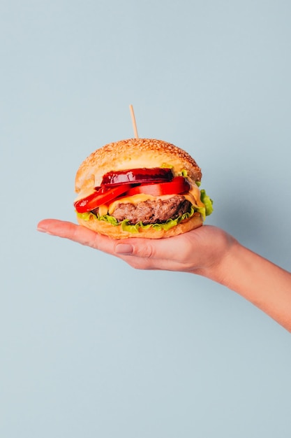 Foto close-up de um hambúrguer na mão de uma mulher em um fundo azul