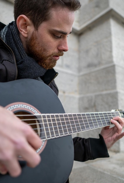 Close-up de um homem barbudo aprendendo a tocar guitarra sozinho em um quadrado vazio Vertical