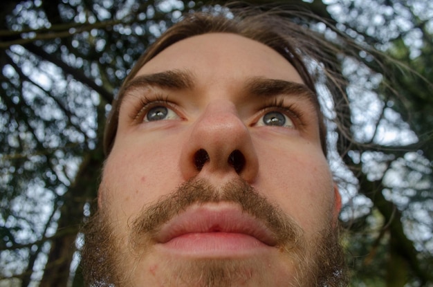 Foto close-up de um homem barbudo contra uma árvore