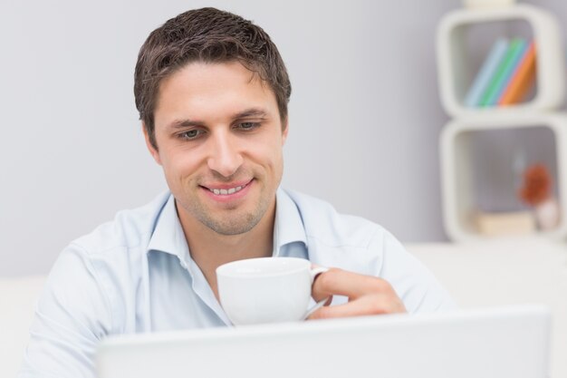 Close-up de um homem com chávena usando laptop em casa