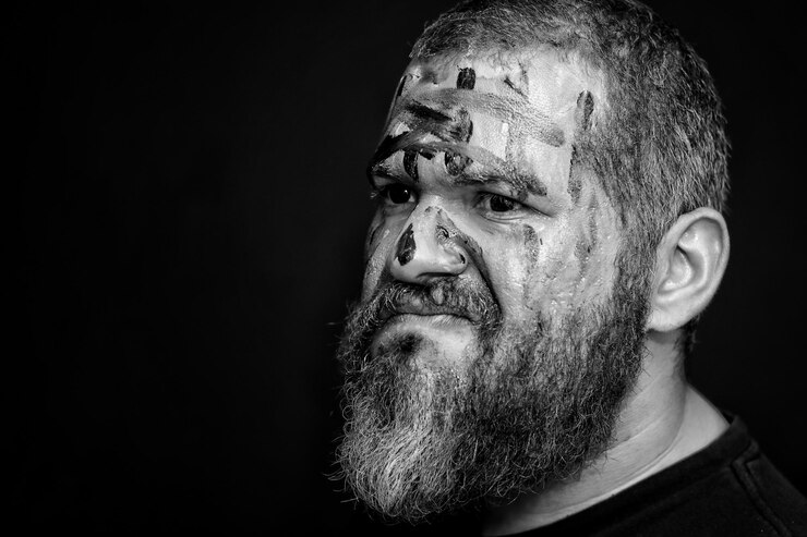 Foto close-up de um homem com tinta no rosto olhando para longe contra um fundo preto