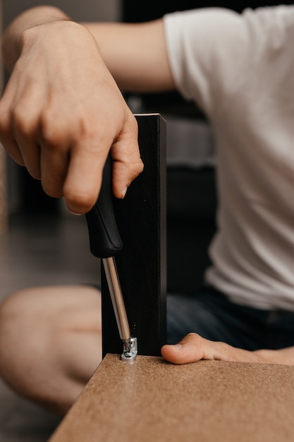 Close-up de um homem consertando uma mesa em sua sala com uma chave de fenda