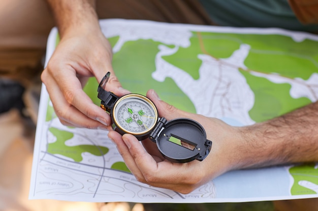 Close-up de um homem irreconhecível segurando a bússola sobre o mapa enquanto procura a rota durante a caminhada, copie o espaço