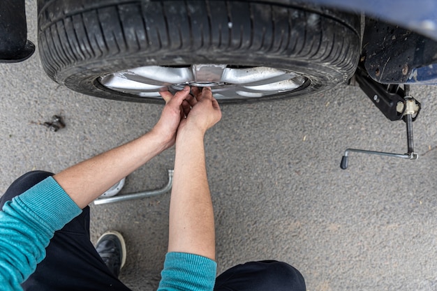 Close-up de um homem muda a roda de um carro na estrada.