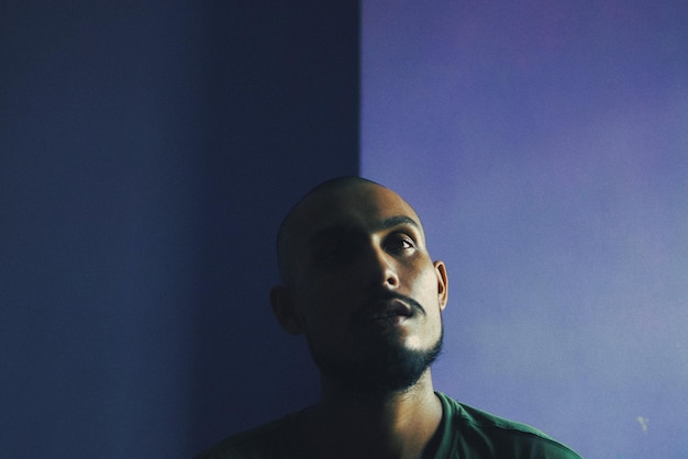 Close-up de um homem pensativo contra a parede azul