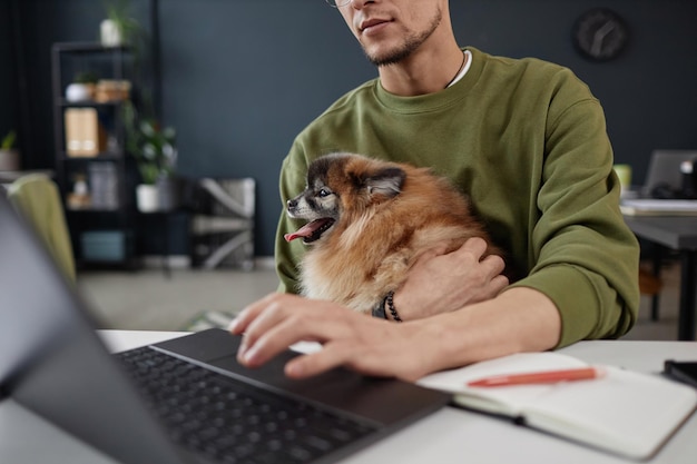 Close-up de um homem segurando um cachorro no colo usando um computador