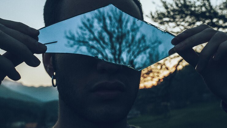 Foto close-up de um homem segurando um espelho quebrado com o reflexo de uma árvore nua nele