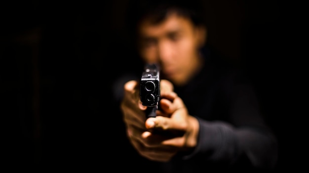 Close-up de um homem segurando uma arma na sala escura