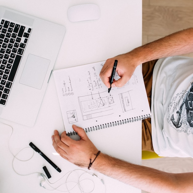 Foto close-up de um homem trabalhando na mesa do escritório, desenhando no bloco de notas