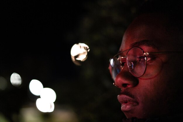 Close-up de um homem usando óculos em uma cidade iluminada à noite