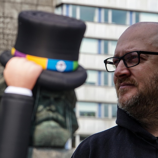 Foto close-up de um homem usando óculos olhando para longe enquanto está de pé contra um edifício na cidade