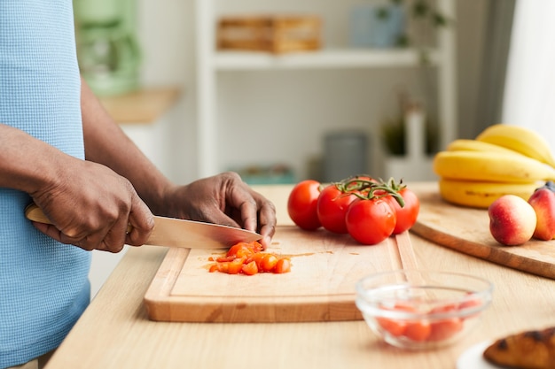 Close-up de um jovem africano cortando tomates em uma tábua na cozinha