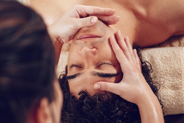 Close-up de um jovem bonito e saudável desfrutando de massagem facial relaxante no salão de beleza. Vista do topo.