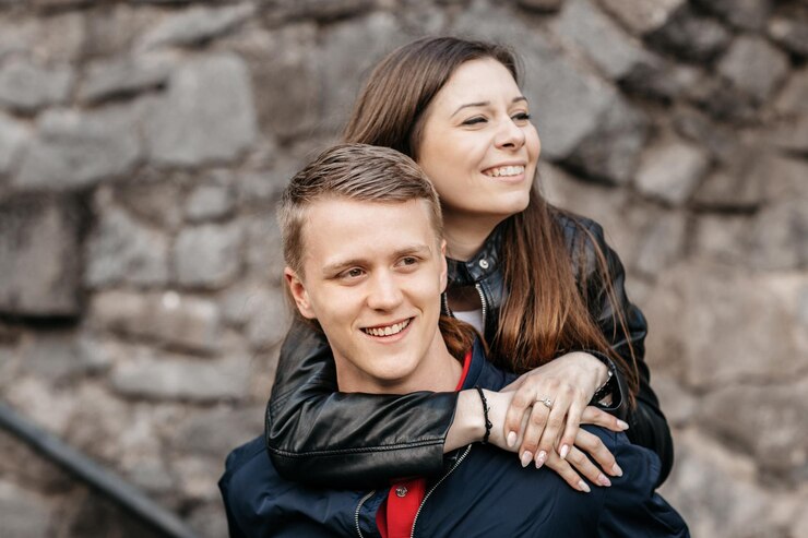 Foto close-up de um jovem casal sorridente olhando para longe enquanto está de pé contra uma parede de pedra