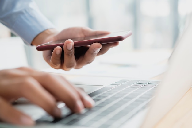 Close-up de um jovem empresário profissional usando smartphone para conectar-se ao computador laptop