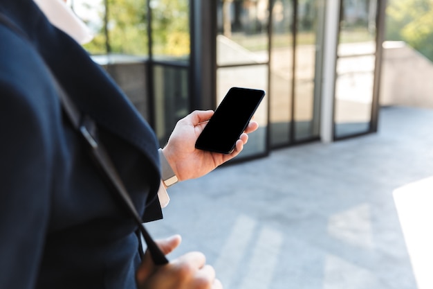 Close-up de um jovem empresário vestindo terno olhando para a tela em branco do celular ao ar livre